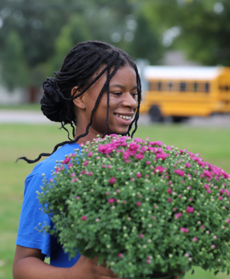  Student carrying mum flowers to plant.